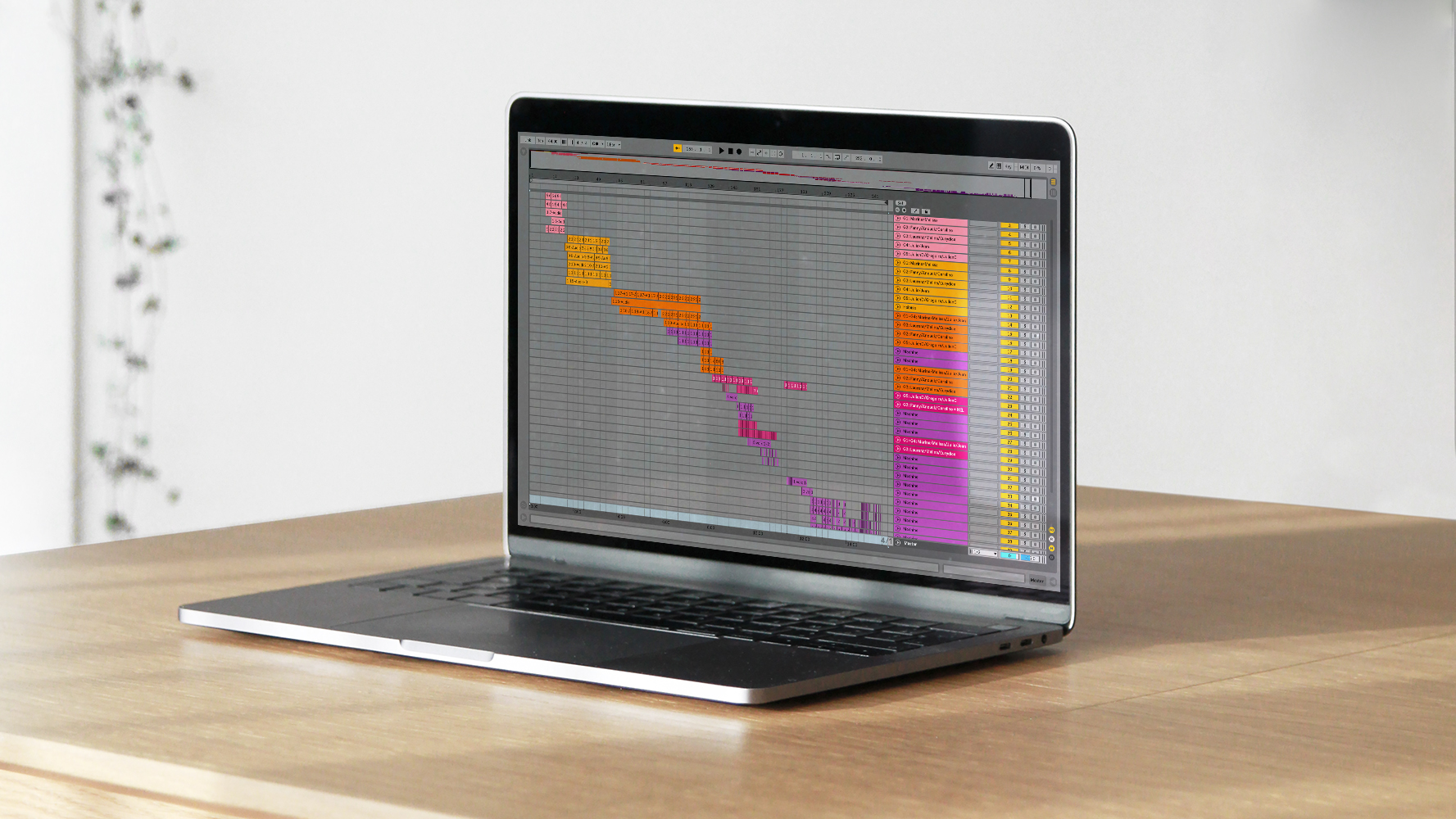 Photographie d'un ordinateur sur une table en bois présentant une capture d'écran du fichier Ableton de la composition musicale Nuit Lavande. Les pistes sonores sont organisées en cascade et par nuances de couleurs du rose au violet.