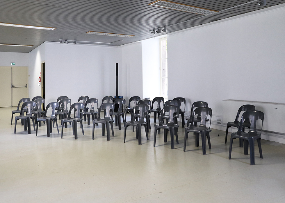 Une quinzaine de chaises vides dans une salle vide.