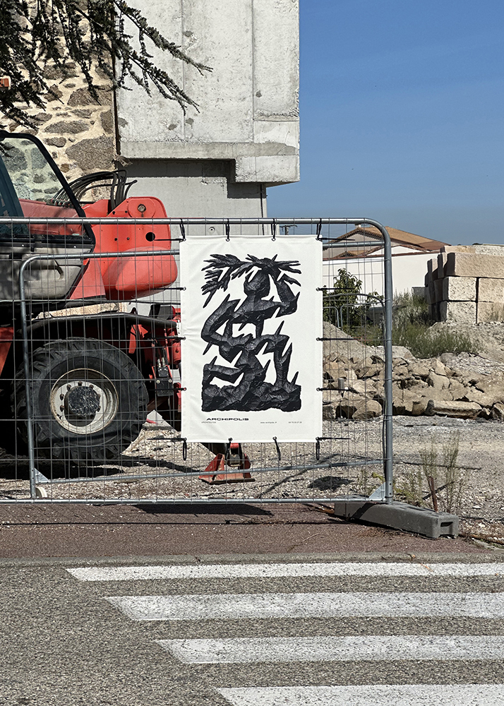 Photographie d'une bâche de chantier avec l'emblème d'Archipolis accrochée à une grille devant un tracteur rouge et une architecture en pierres.