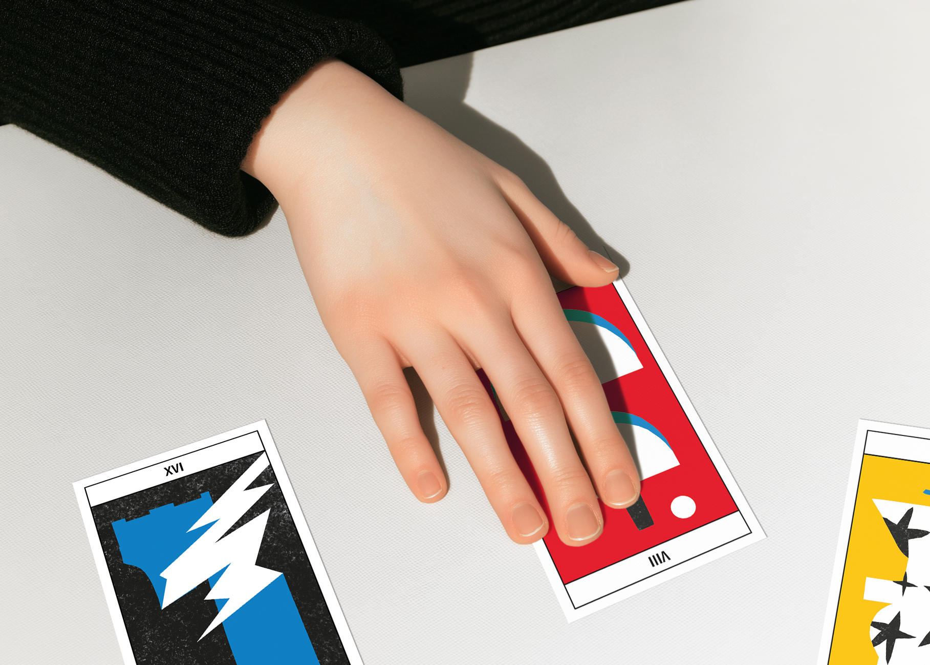 Main droite qui tire la carte Balance, numéro 8 du jeu de tarot Pompidou. Deux autres carte sont éparpillées sur la table, l'étoile et la tour.