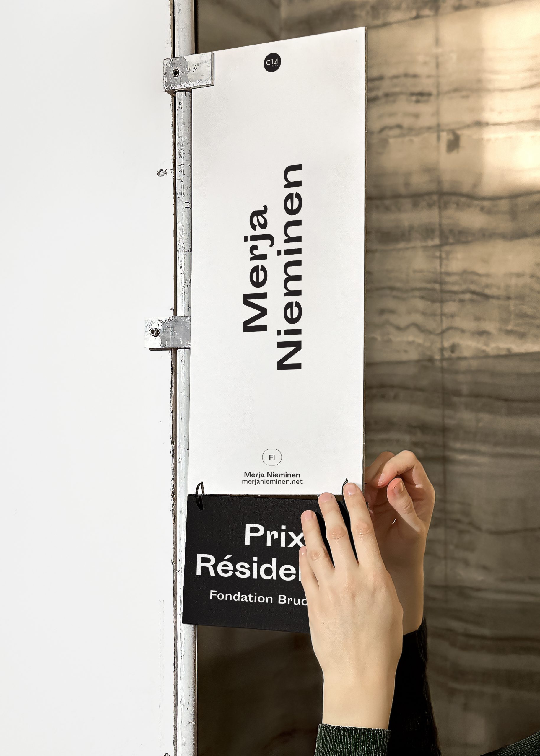 Détail du cartel de Merja Nieminen. Des mains sont en train d'accrocher le label (Prix Résidence) au cartel.